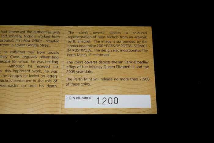 A close-up of a wooden display plaque with printed text about a coin, including the text 'COIN NUMBER 1200', photographed against a dark background.
