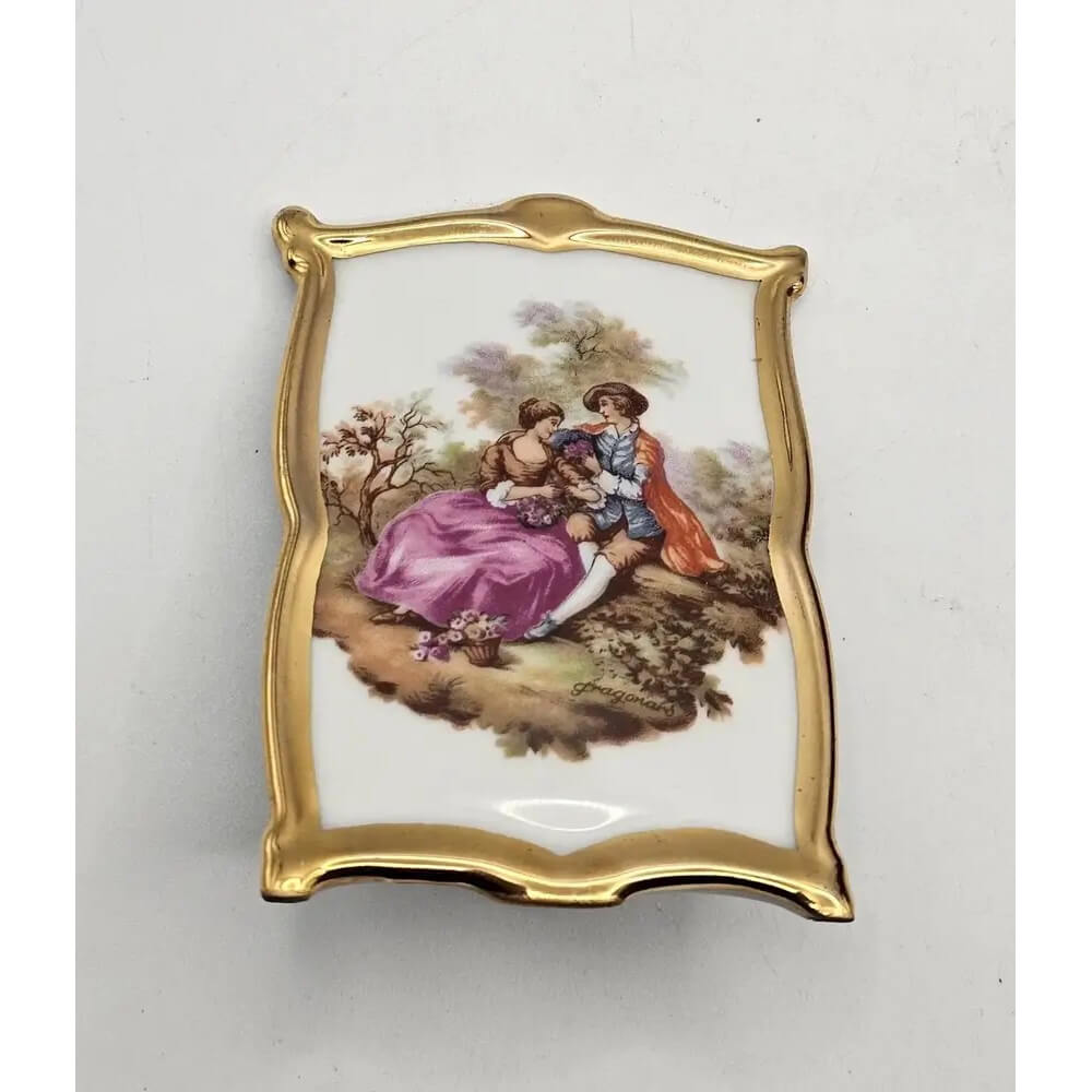 Decorative plaque with a gold frame and painted scene of two people in a garden on a white background