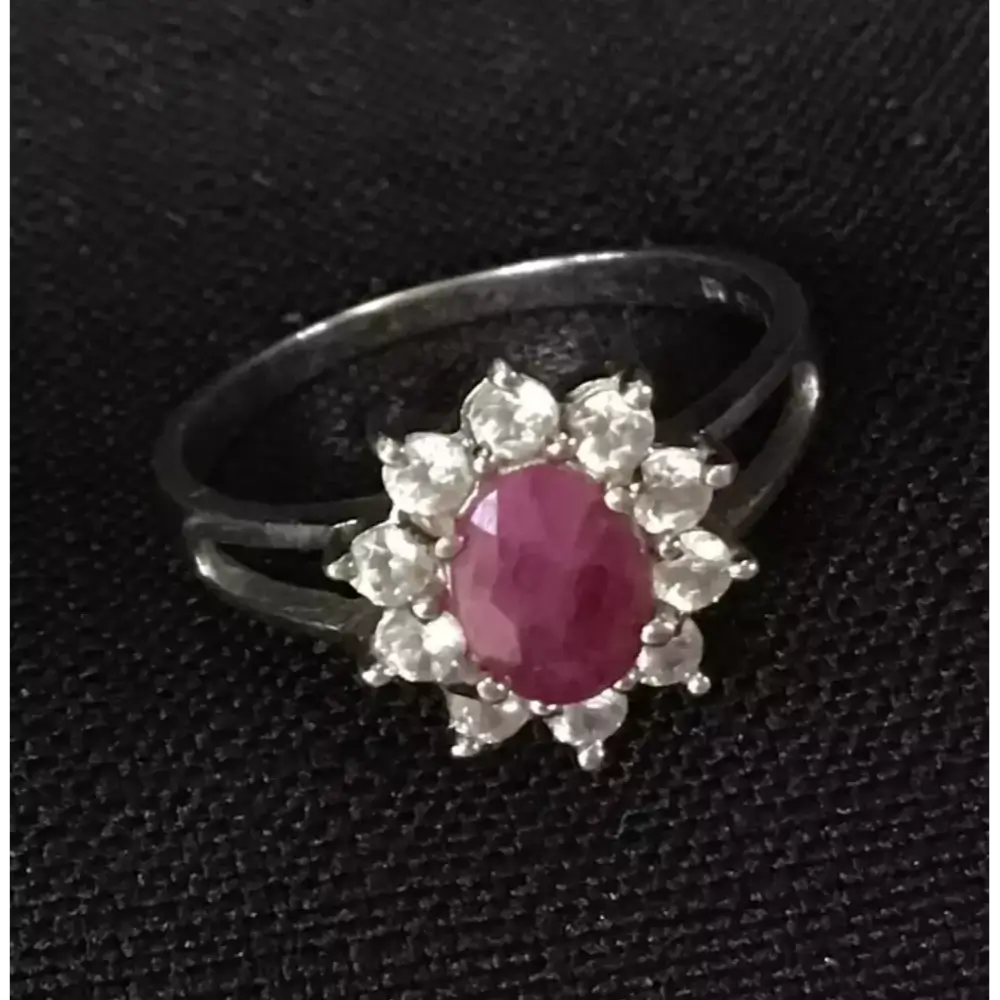 Silver ring with a red gemstone and smaller diamonds on a black background