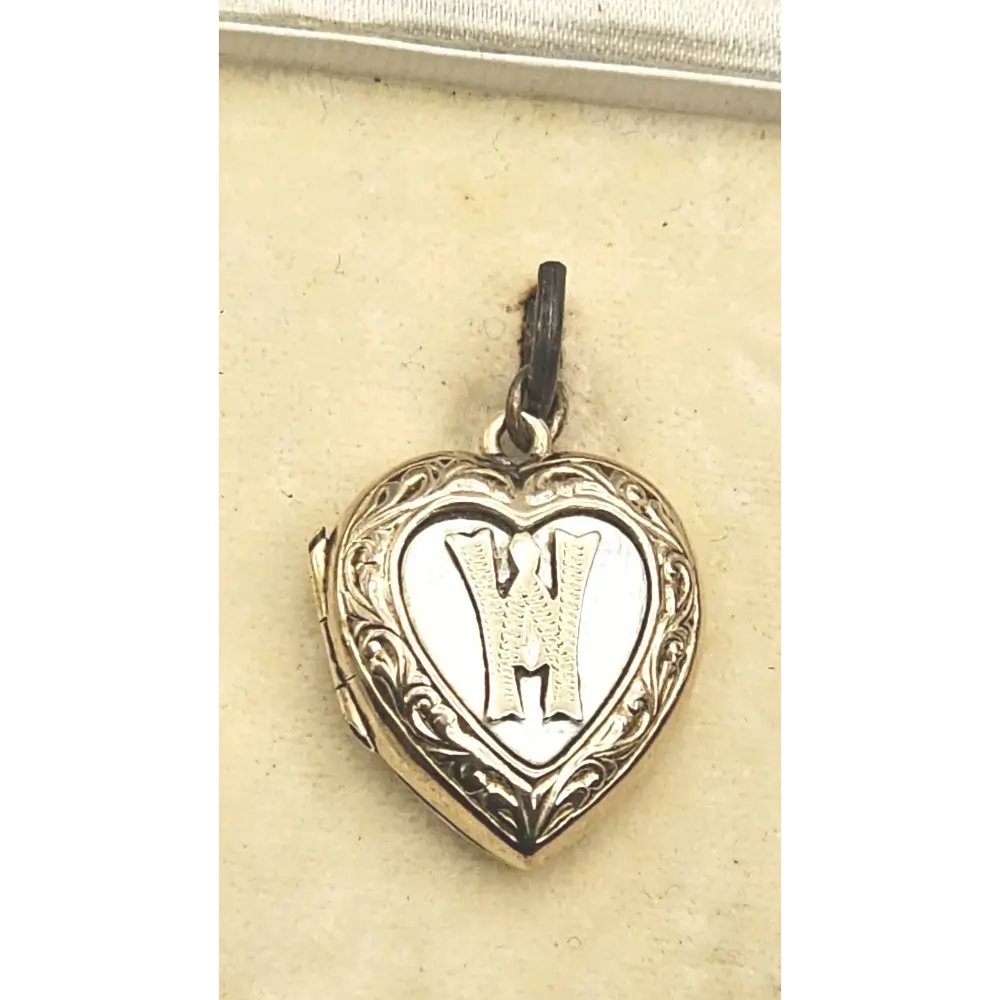 Heart-shaped locket with engraved design and letter 'H' on a beige card