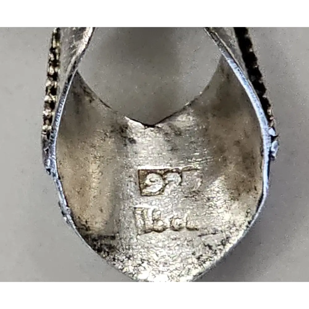 Close-up of a silver pendant with '925' stamp on a gray background