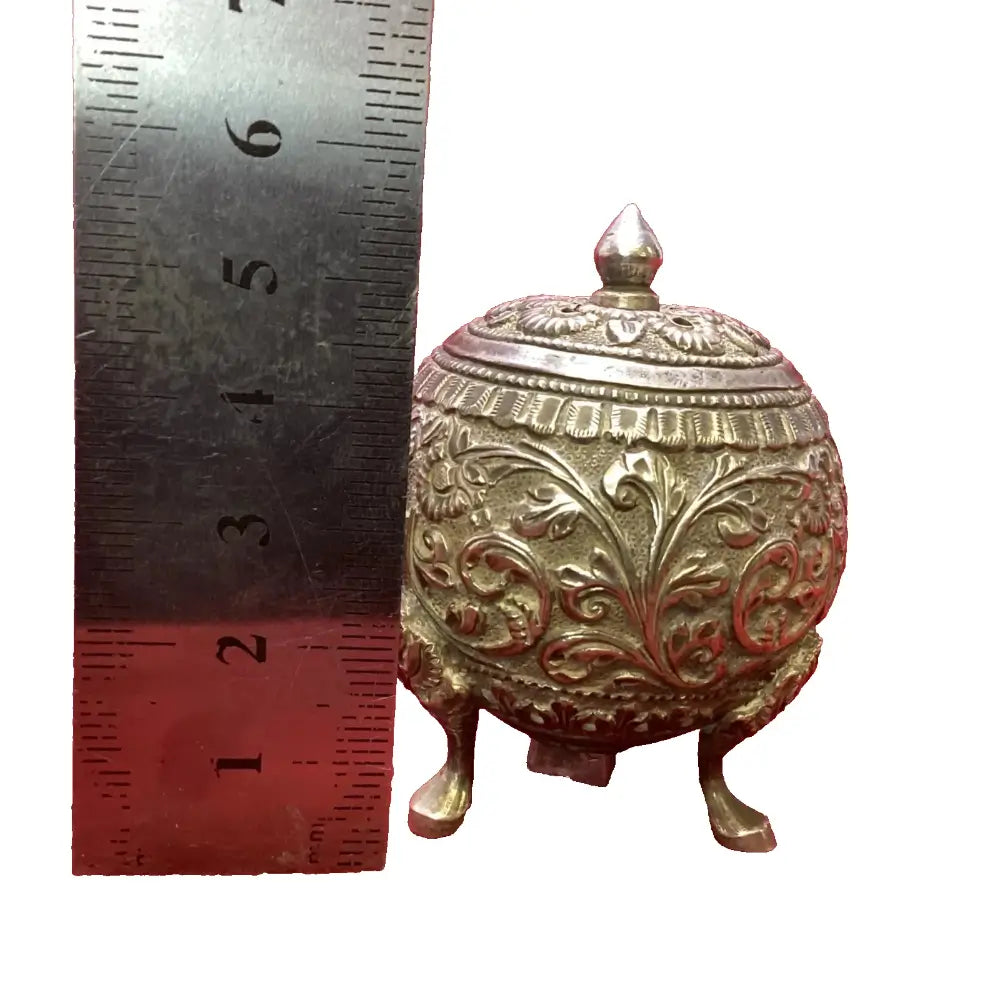 Decorative brass container with intricate designs next to a ruler for scale