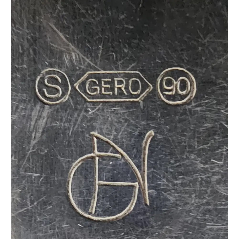 Close-up of engraved marks on a metallic surface, including 'S', 'GERO 90', and a signature.