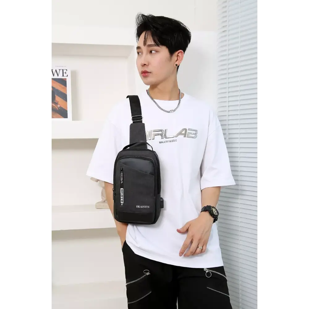 Person wearing a white t-shirt with a brand logo and carrying a black sling bag