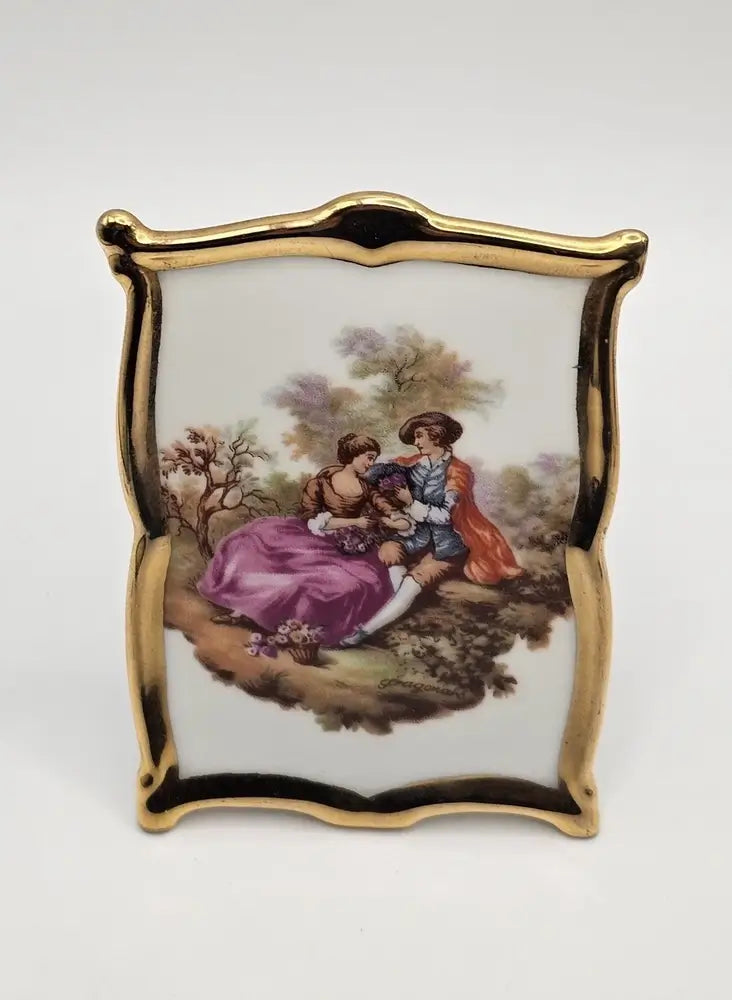 Decorative piece with a gold frame and painting of a couple in a garden