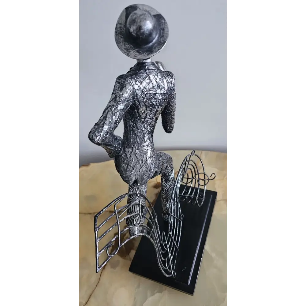 Metallic sculpture of a figure with a hat on a stand against a light background