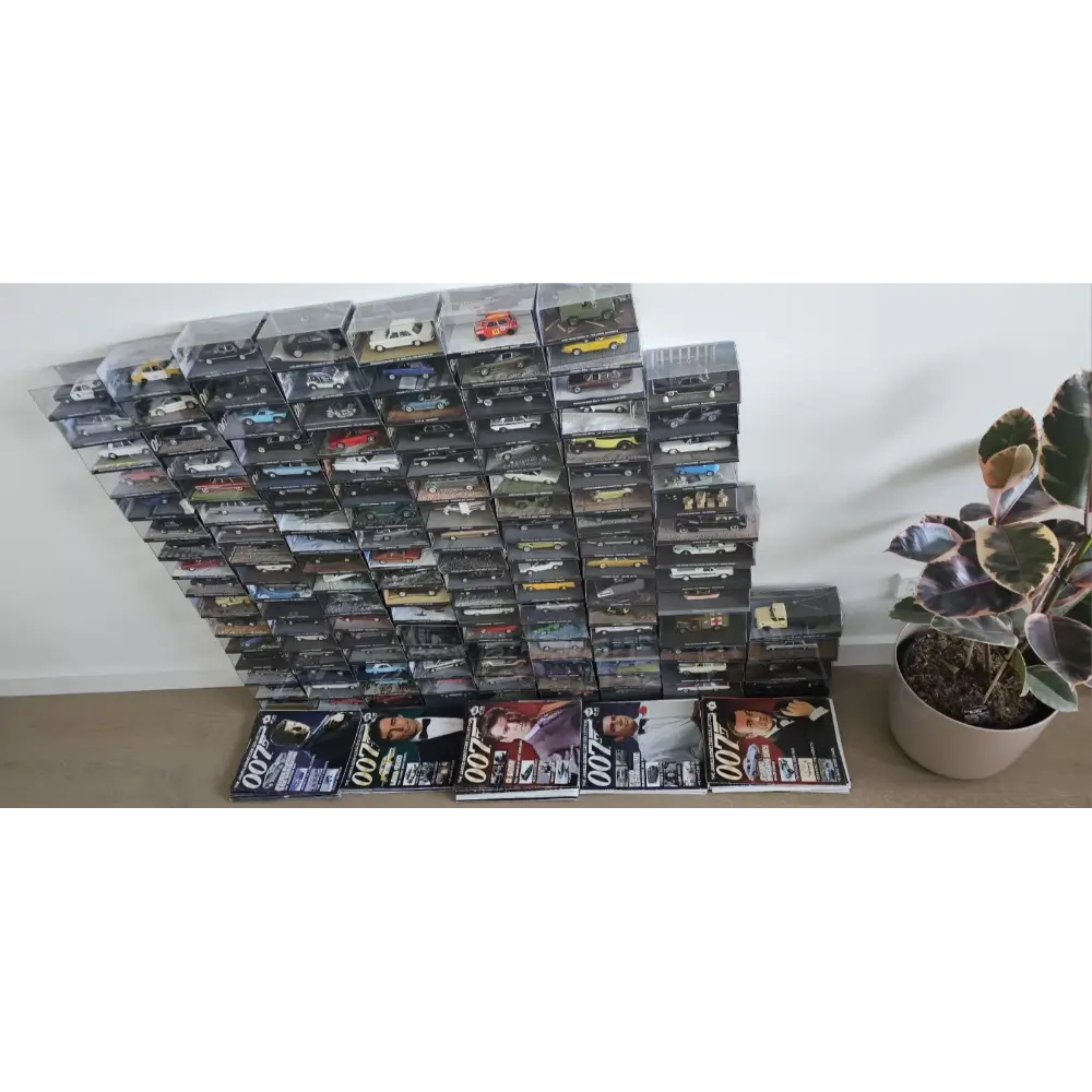 Collection of model car boxes stacked on a surface with a plant in the background.