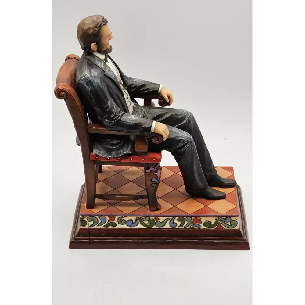 Statue of a man sitting on a chair with a decorative base on a white background