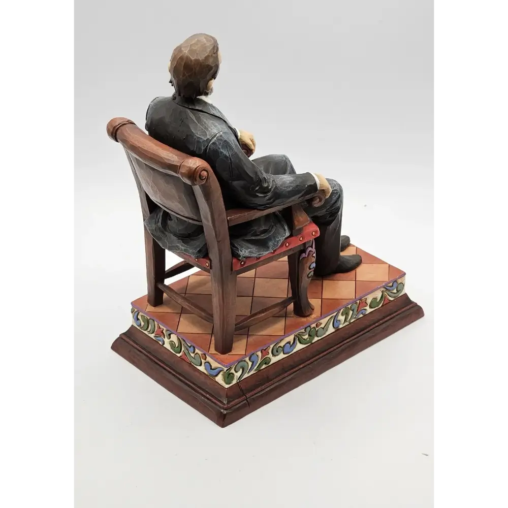 Statue of a person sitting on a chair with a decorative base on a white background