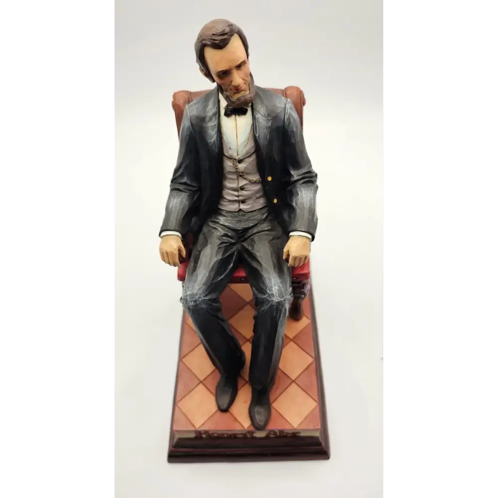 Statue of a man in formal attire sitting on a chair with a checkered floor background