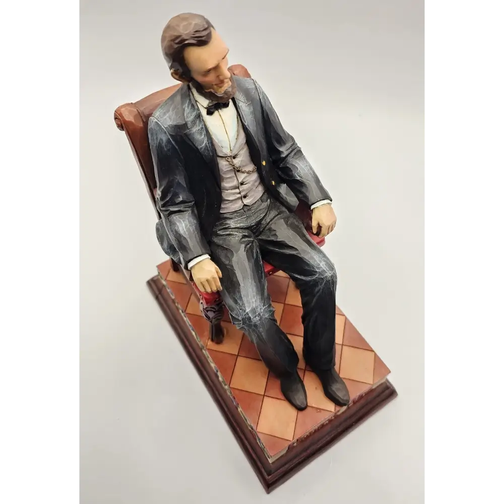 Statue of a man in formal attire sitting on a chair with a checkered floor background