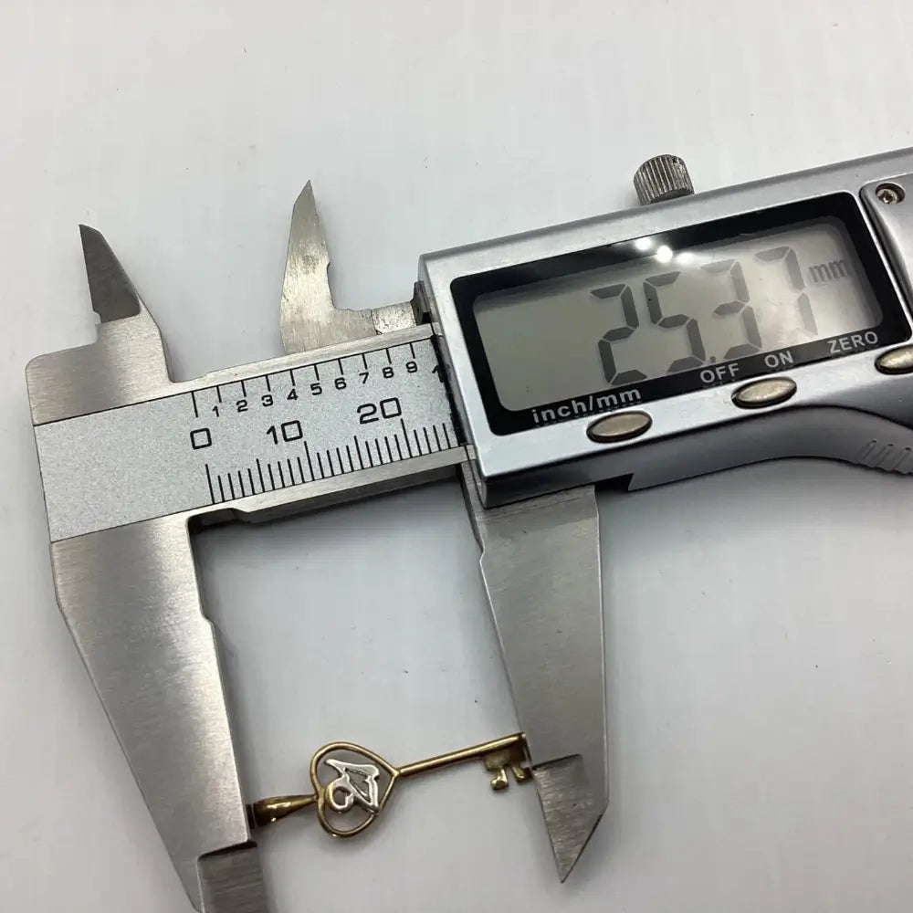 Digital caliper measuring a gold key charm against a white background