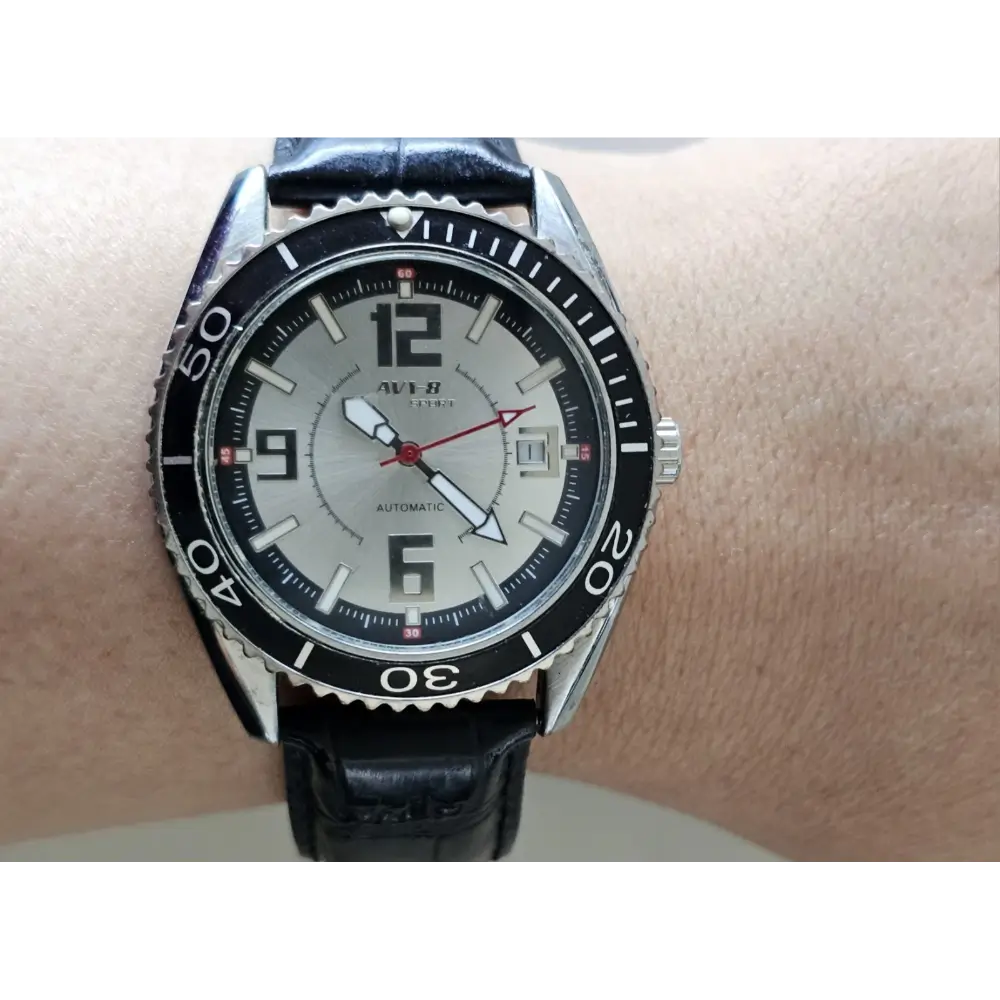 Black wristwatch with a silver bezel on a wrist against a neutral background