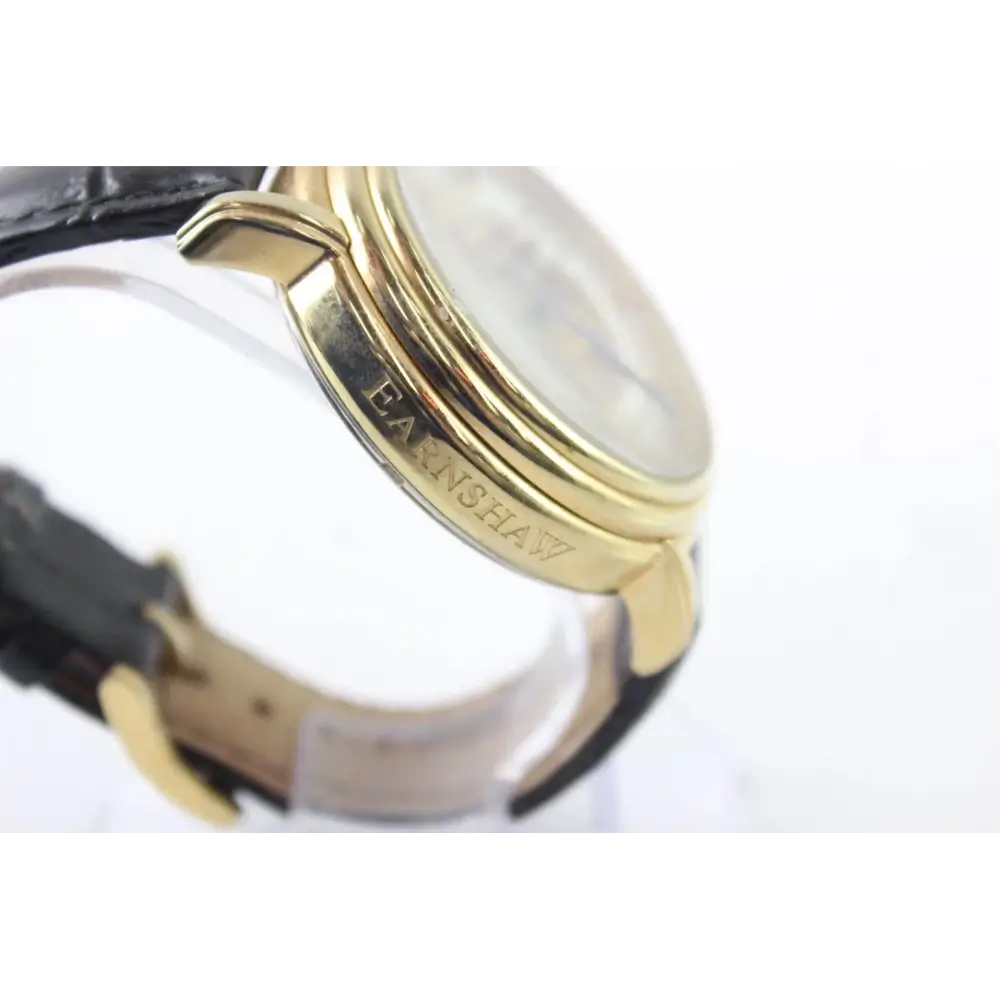 Close-up of a watch with a gold bezel and black strap