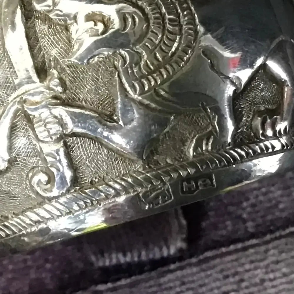 Close-up of a silver belt buckle with intricate designs on a textured surface.