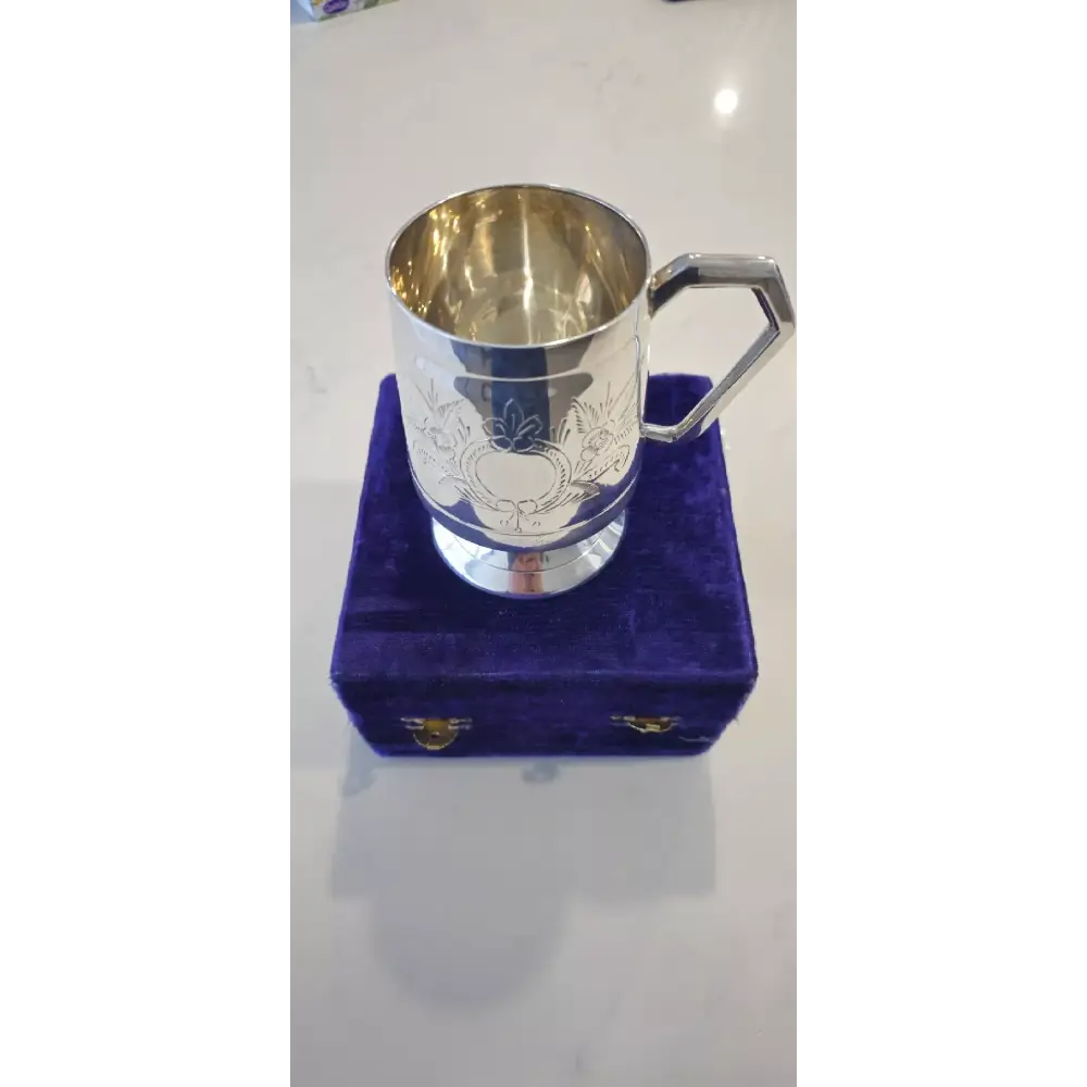 Silver cup with engraved design on a purple cushioned stand