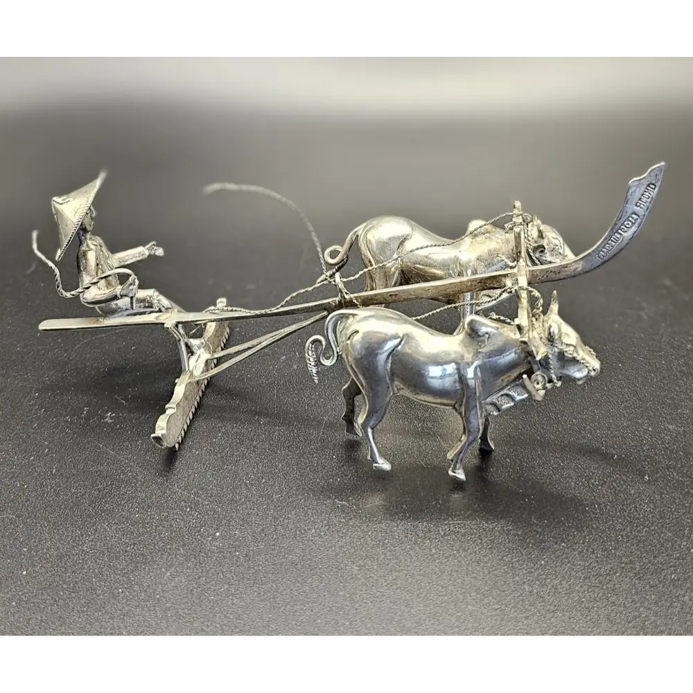 Silver sculpture of a farmer on a cart pulled by two oxen on a dark surface