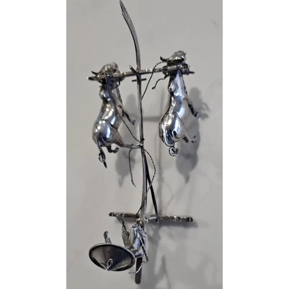Metallic sculpture of three figures on a branch against a light gray background