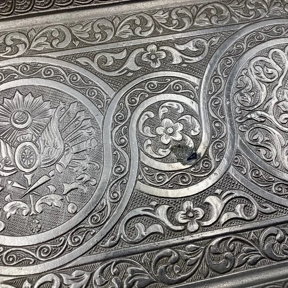 Close-up of intricate silver embossing with floral and geometric patterns.