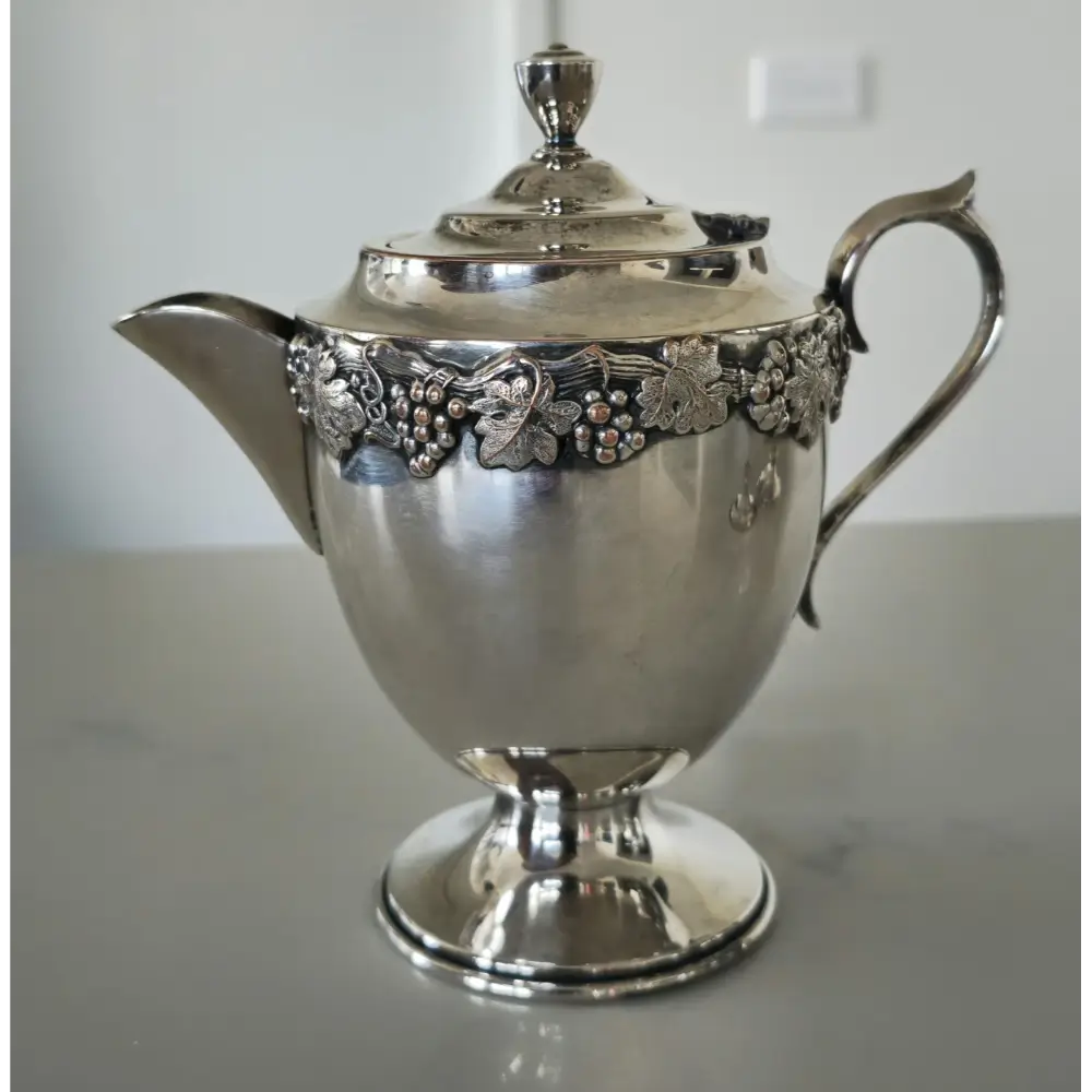 Silver teapot with floral embellishments on a reflective surface