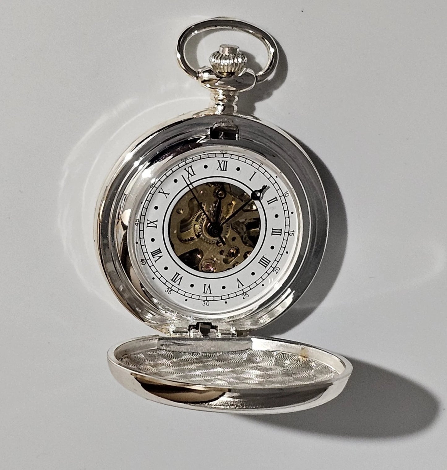 Silver pocket watch with open face on a light gray background