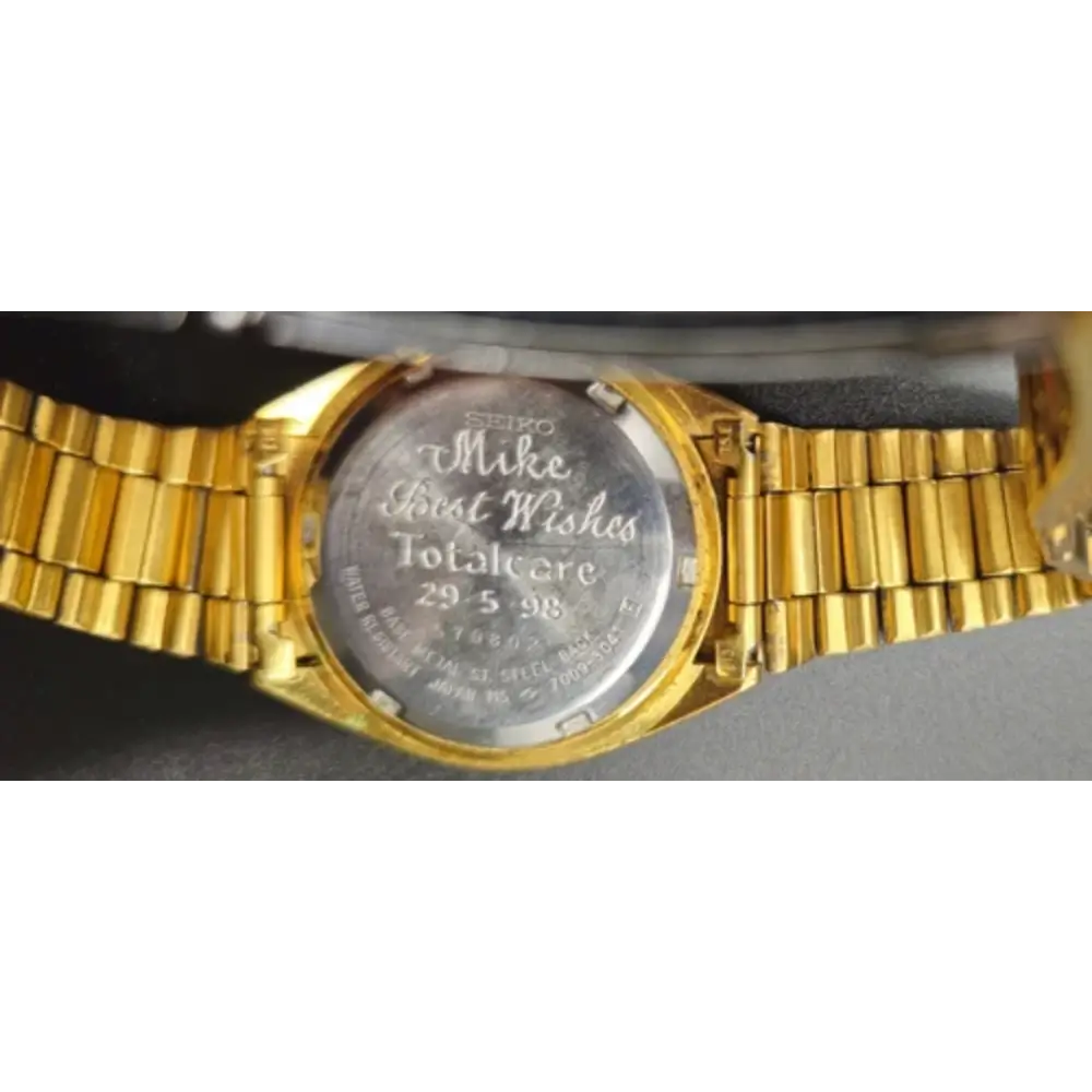 Gold wristwatch with engraved text on a gray background