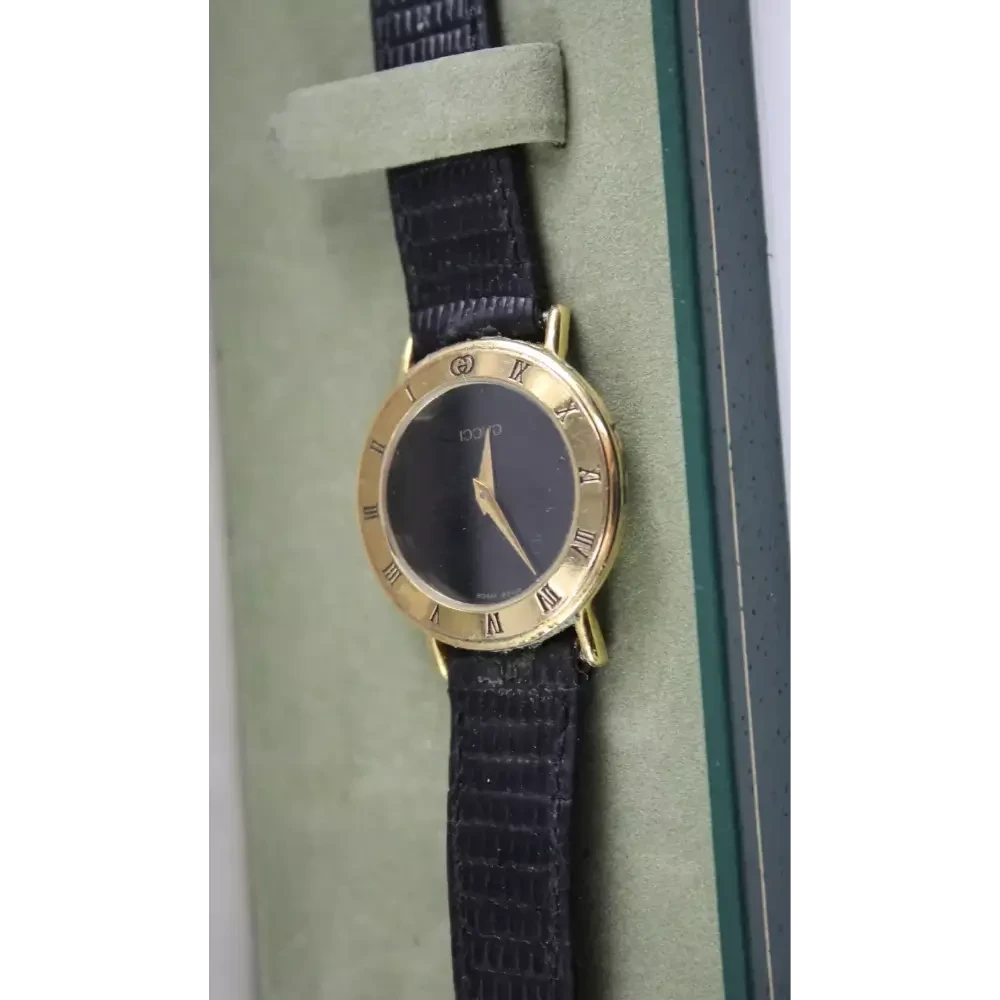 Gold watch with a black strap on a green cushion