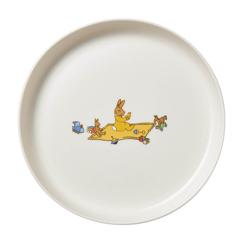 A round off-white ceramic plate featuring a small colorful illustration in the center of rabbits playing with toys on a yellow blanket.