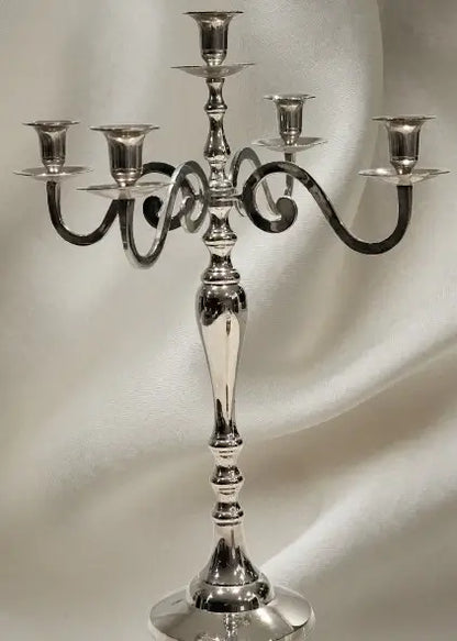 A polished silver five-arm candelabra with a fluted stem and circular base, set against a draped white fabric background.