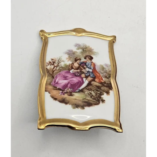 Decorative plaque with a gold frame and painted scene of two people in a garden on a white background