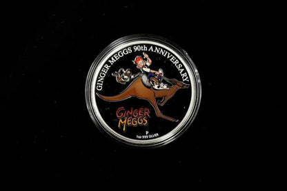 A round silver commemorative coin or medallion on a black background, featuring an illustration of a person riding a kangaroo with the text 'GINGER MEGGS 90TH ANNIVERSARY' and 'GINGER MEGGS'.