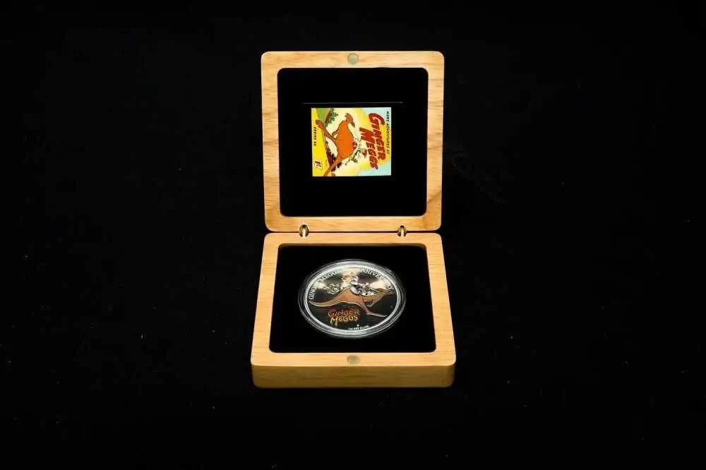 A collectible silver coin displayed inside an open light wood presentation box with black velvet lining, set against a solid black background.
