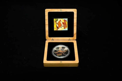 A collectible silver coin displayed inside an open light wood presentation box with black velvet lining, set against a solid black background.