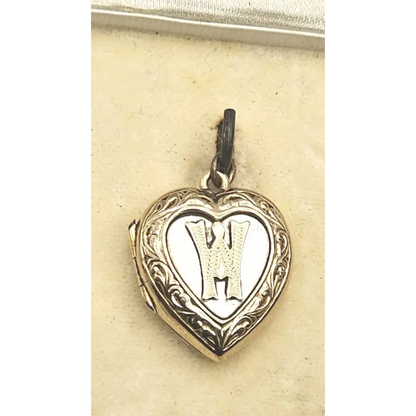 Heart-shaped locket with engraved design and letter 'H' on a beige card