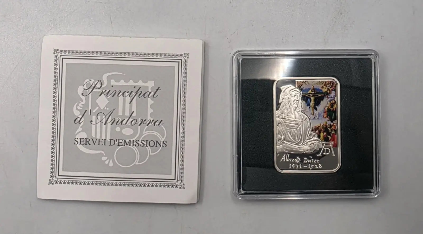 A silver-colored religious medal from the Principat d'Andorra, dated 1911-1939, displayed next to its white presentation card on a gray background.
