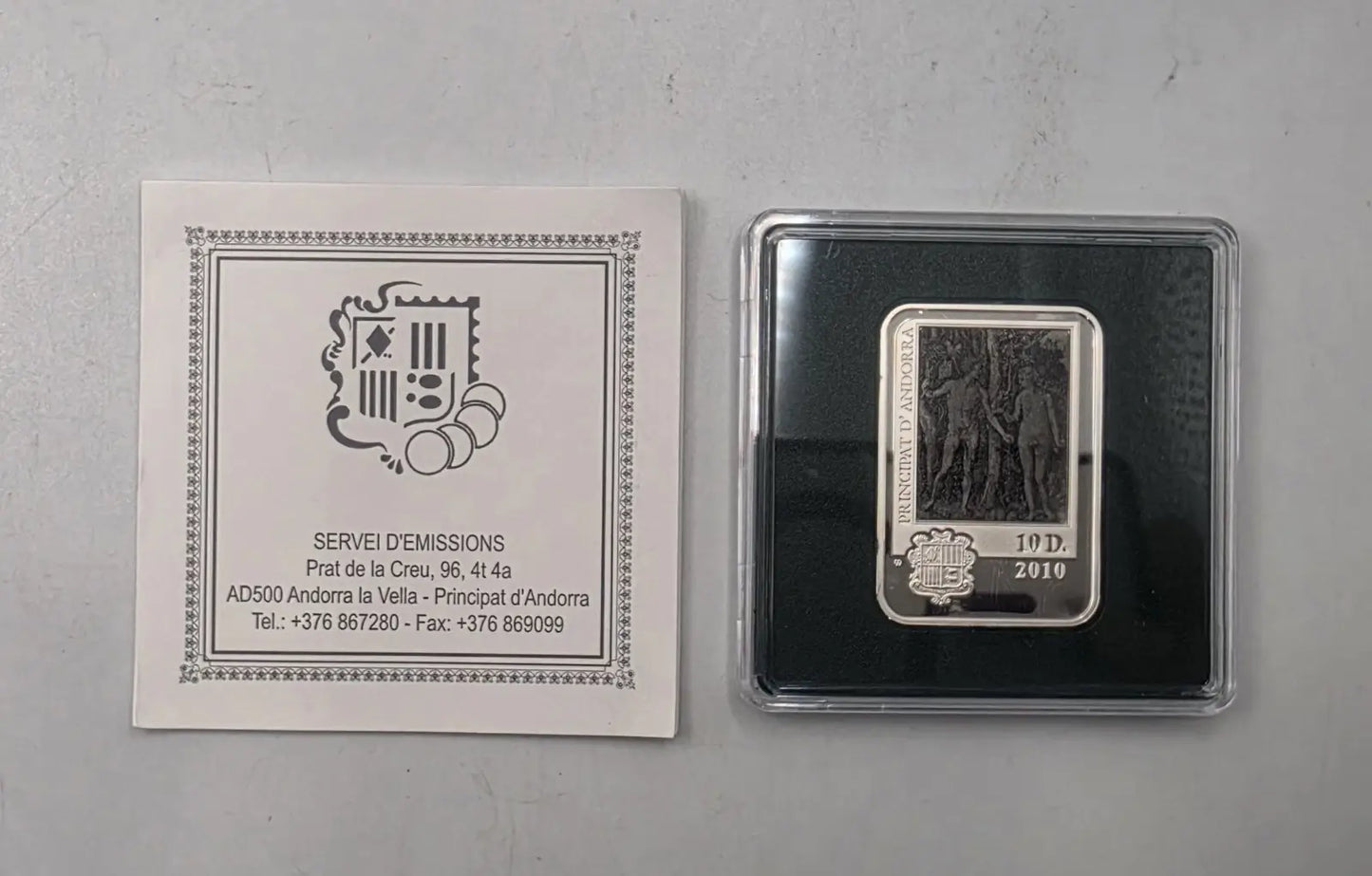 A 10 dimes 2010 silver coin from Andorra, displayed next to its original white paper certificate insert on a light gray surface.