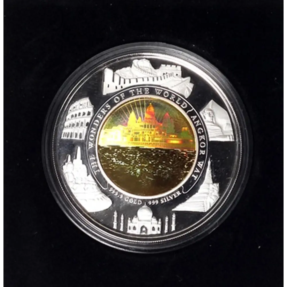 A circular collectible coin in a clear protective capsule, featuring a gold-toned central medallion with a domed building and surrounding silver-toned border illustrations of world landmarks, including the Colosseum, Taj Mahal, and Great Wall. Text on the coin reads 'WONDERS OF THE WORLD / ARGXOR WAY' and '2500 GOLD / 999 SILVER'.