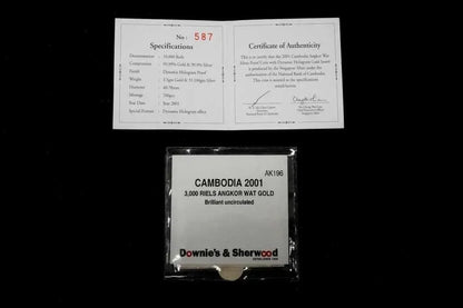 A packaged gold coin from Cambodia, 3,000 Reils Angkor Wat Gold, shown below its authenticity certificate and specifications card on a black background. The coin is sealed in a clear plastic bag with a white label, and the certificate is printed on white paper.