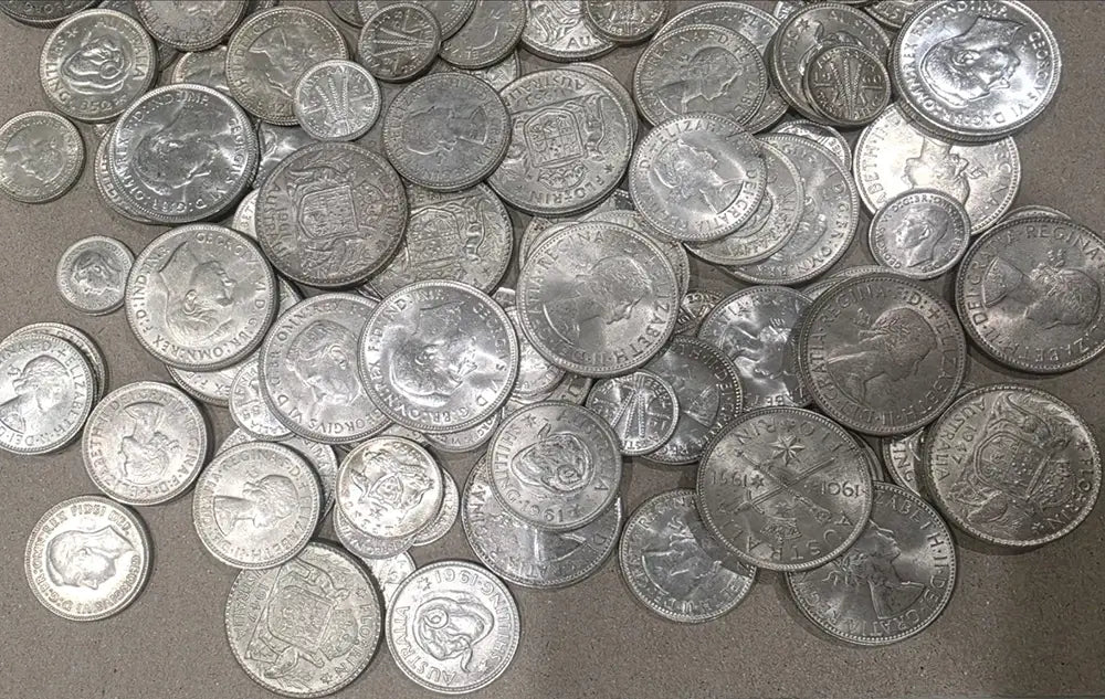 A pile of vintage silver coins, including Buffalo nickel and dime-sized pieces, scattered on a neutral gray surface.