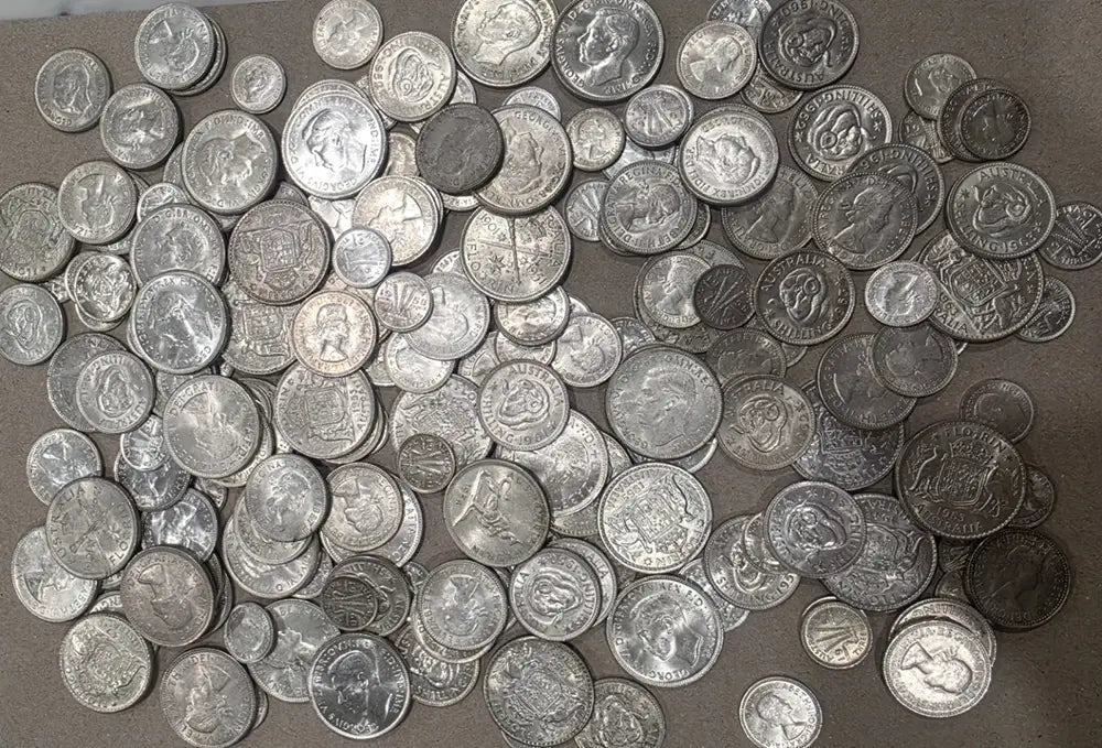 A large pile of assorted silver-colored coins spread across a brown surface.