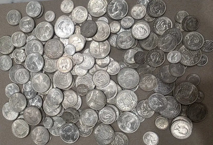 A large pile of assorted silver-colored coins spread across a brown surface.