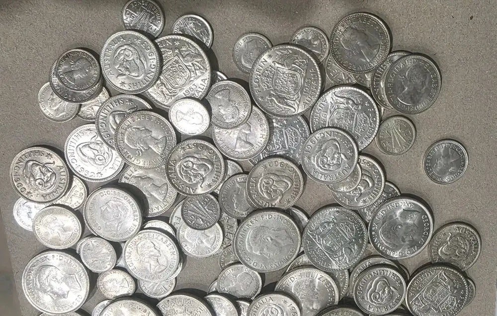 A pile of silver-colored coins scattered on a neutral gray surface.