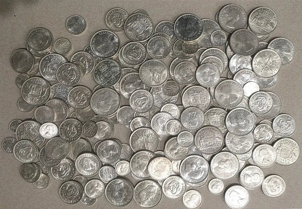 A pile of assorted silver-colored coins scattered across a neutral gray surface.