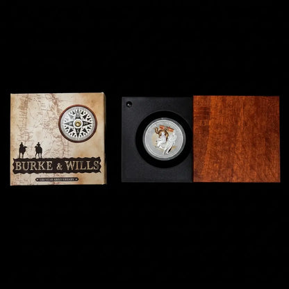 A collectible coin presentation set for Burke & Wills, featuring a vintage-style illustrated box on the left and a black display case with a silver coin mounted on the right, next to a reddish-brown wood panel from our World & Vintage Coins collection 