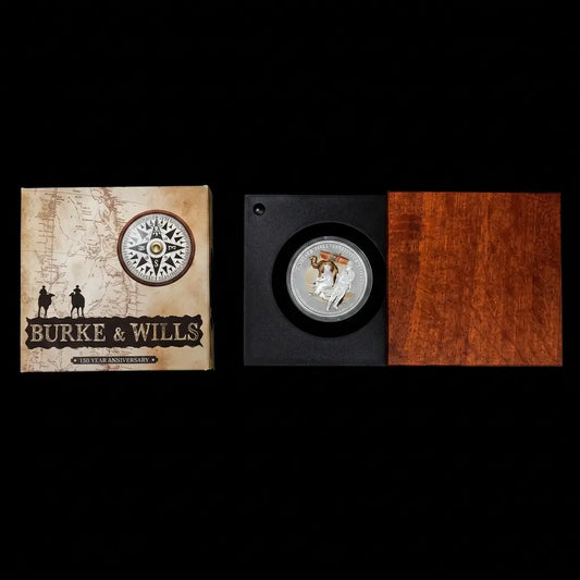 A collectible coin presentation set for Burke & Wills, featuring a vintage-style illustrated box on the left and a black display case with a silver coin mounted on the right, next to a reddish-brown wood panel from our World & Vintage Coins collection 