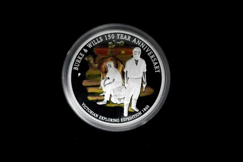 A circular commemorative coin or medallion with a silver-toned rim, featuring a black background and white text reading 'BURE & WILLS 150 YEAR ANNIVERSARY' and 'VICTORIAN EXPLORING EXPEDITION 1848,' with an illustrated scene in the center. The coin is photographed against a solid black background.