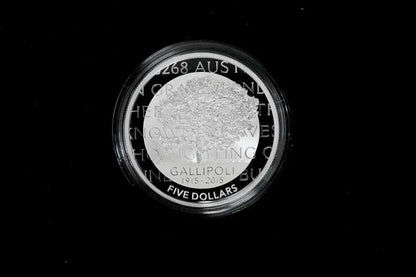 A circular silver coin with a clear protective plastic capsule, featuring the text 'GALLIPOLI 2015-2026 FIVE DOLLARS' and a textured central design, set against a solid black background.
