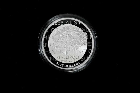 A circular silver coin with a clear protective plastic capsule, featuring the text 'GALLIPOLI 2015-2026 FIVE DOLLARS' and a textured central design, set against a solid black background.