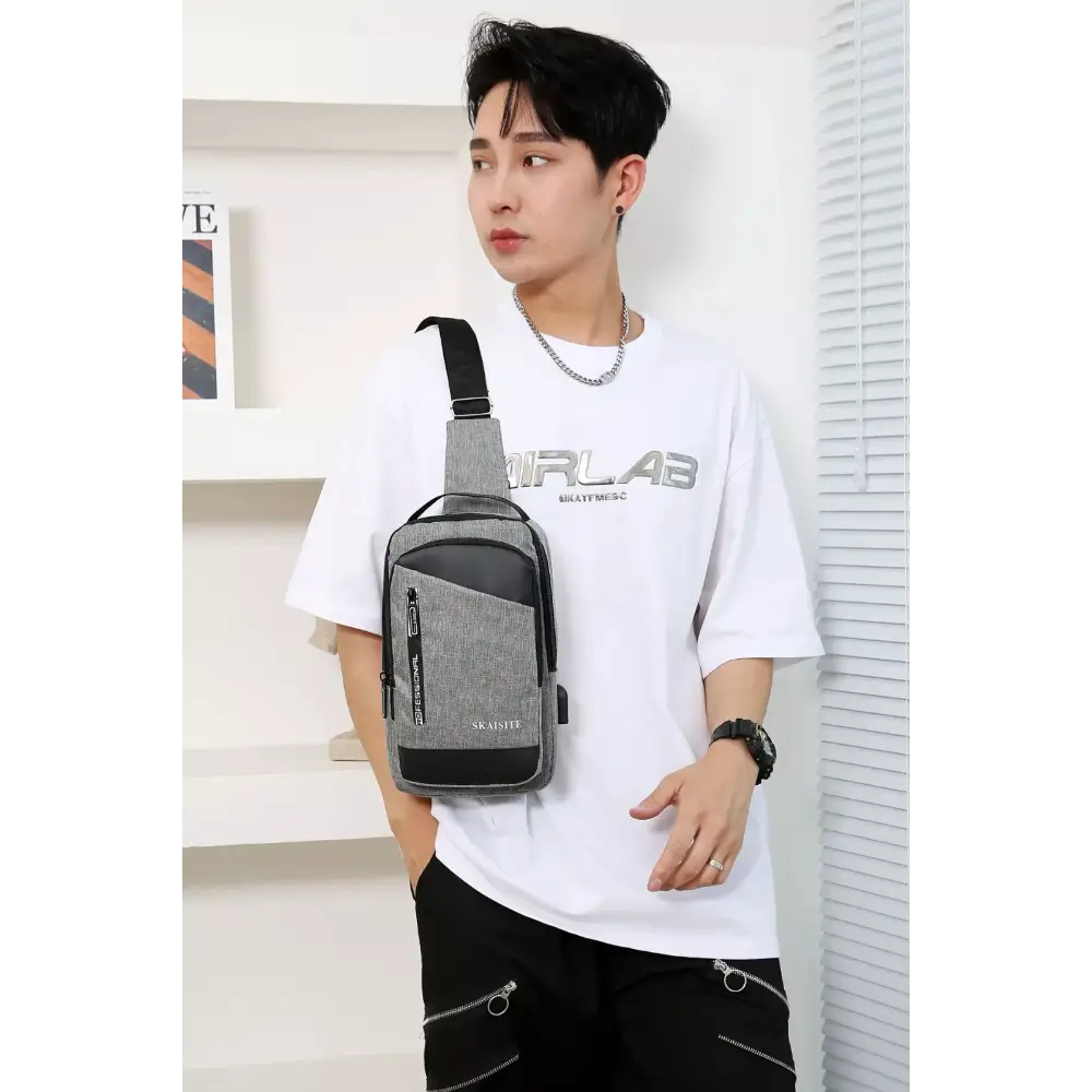 Person wearing a white t-shirt with a brand logo and carrying a  sling gray crossbody bag.
