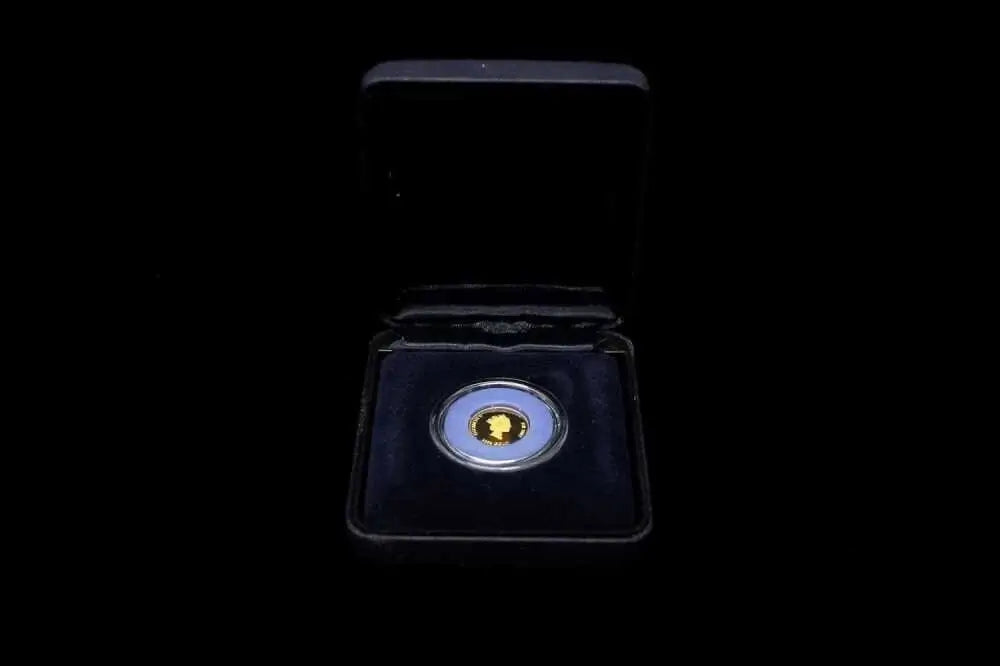 A small round coin or medallion with a gold-toned center and blue outer ring, displayed inside an open black presentation box on a black background.